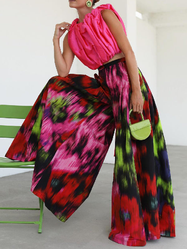 Woman wearing Wide Leg Printed Pants in vibrant multi-colored print with a pink top and green handbag.